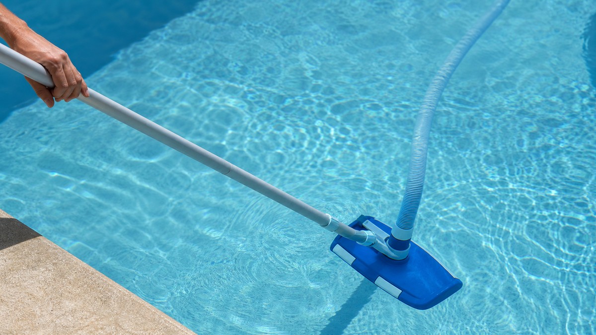 Limpiafondos manual con cabezal y pértiga aspirando el fondo de una piscina residencial